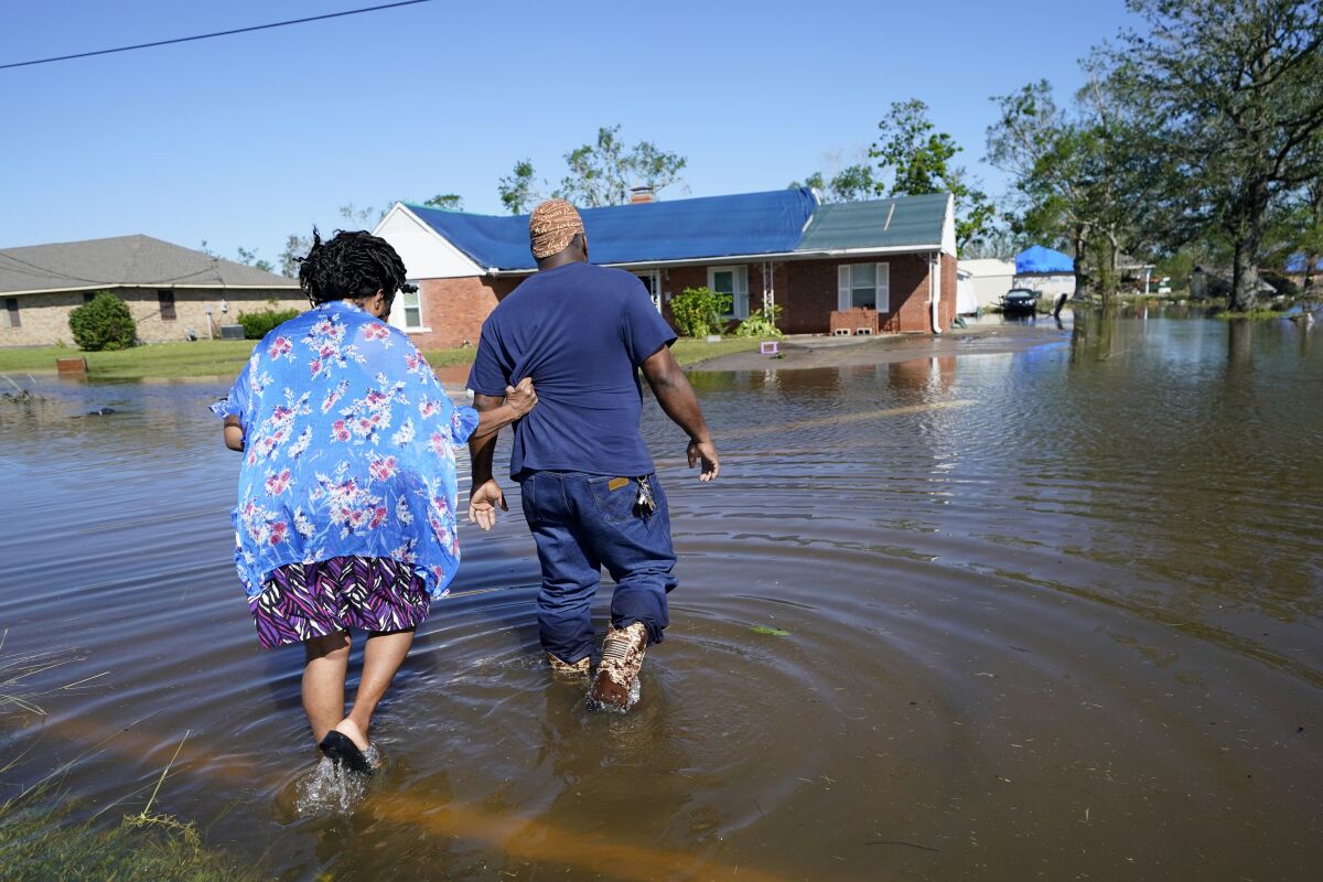 FILE - Soncia King holds onto her husband, Patrick King, in Lake Charles, La., Saturday, Oct. 10, 2020, as they walk through the flooded street to their home, after Hurricane Delta moved through the previous day. According to a study published in Nature Communications on Tuesday, April 12, 2022, climate change made the record-smashing deadly 2020 Atlantic hurricane season noticeably wetter. (AP Photo/Gerald Herbert, File)