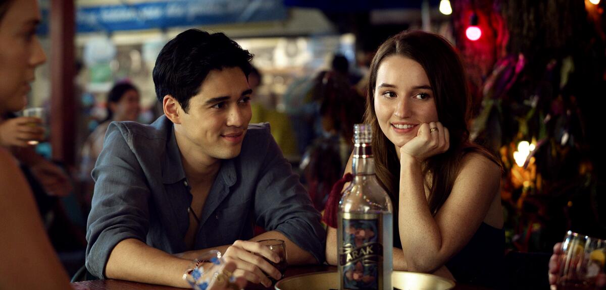 A young man and woman sit at a table with a bottle of alcohol.