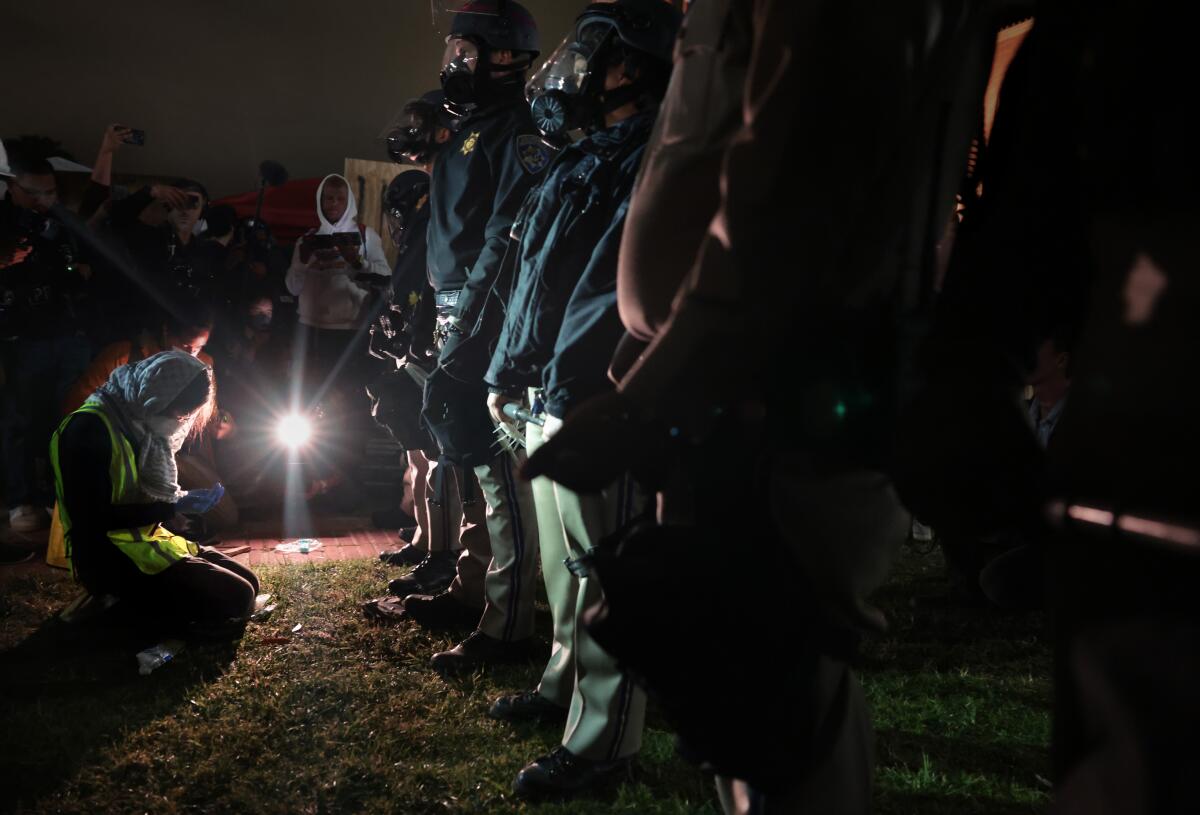 A woman kneels in front of a row of law enforcement officers.