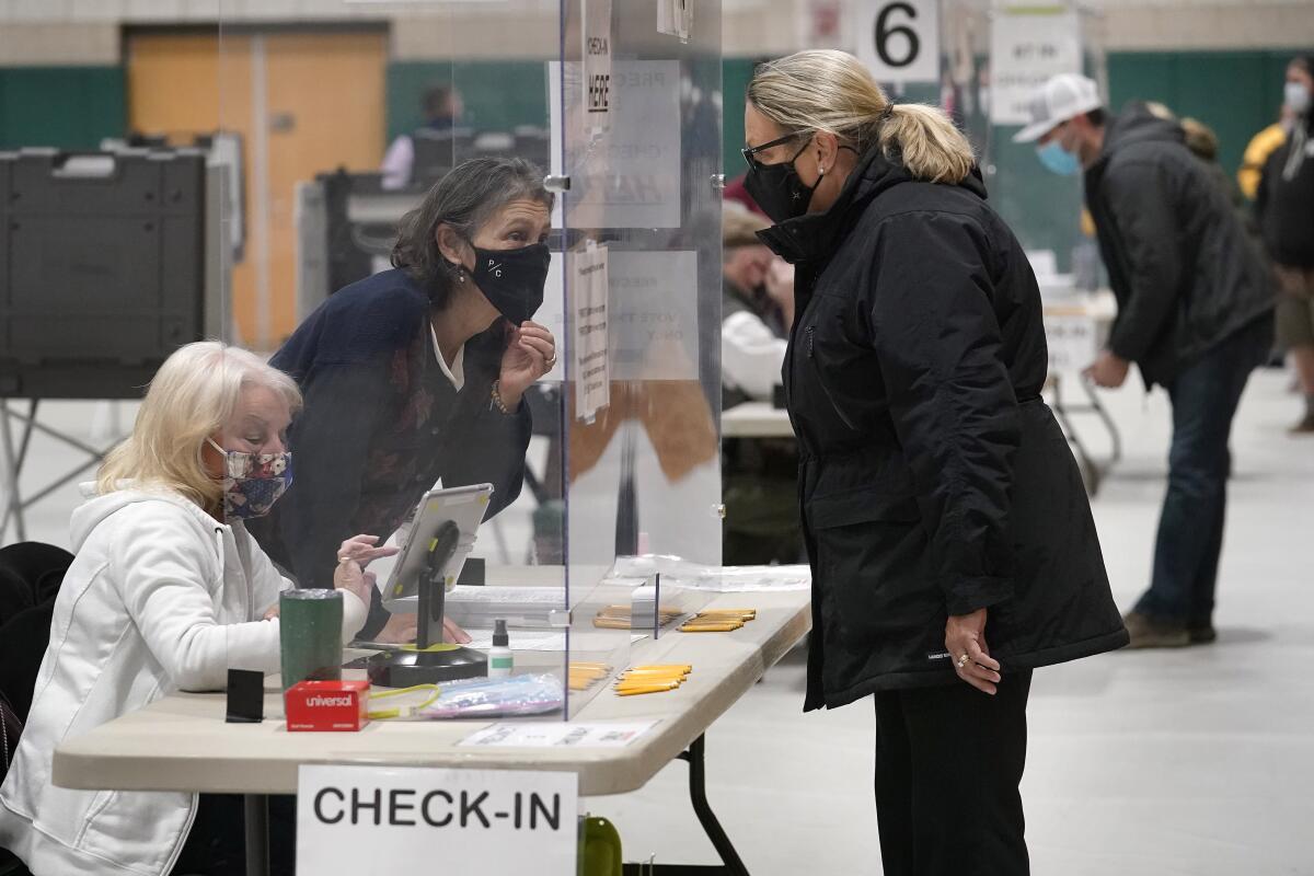 A poll worker speaks through a plastic barrier while assisting a voter in a polling station in Marshfield, Mass. 