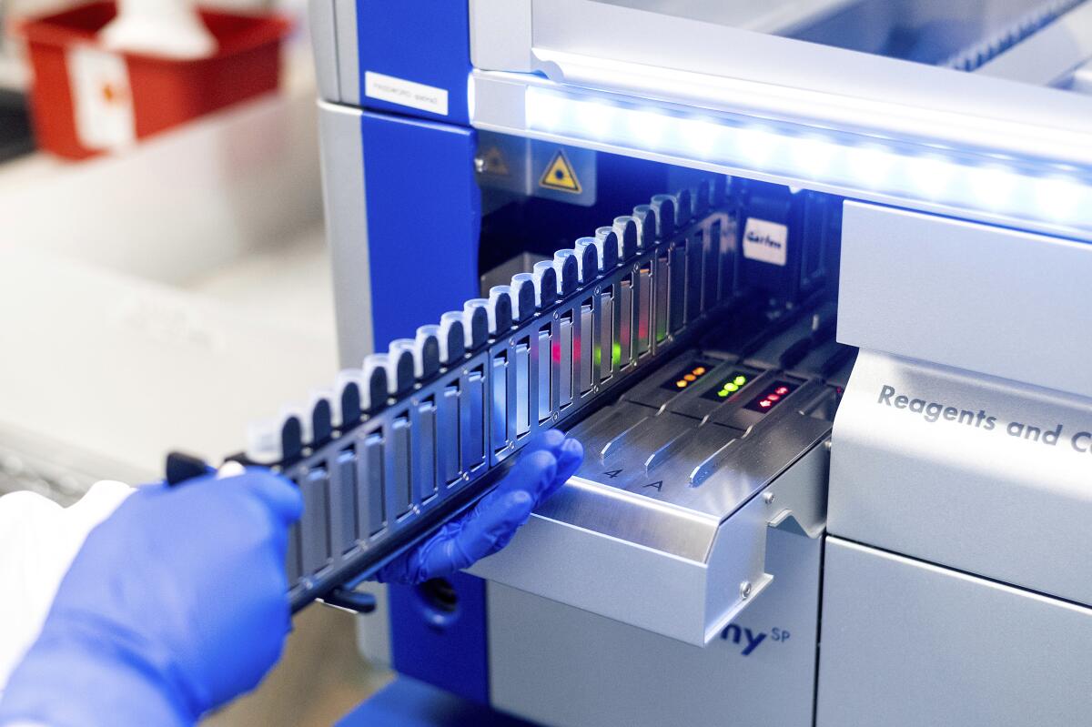 Gloved hands hold a rack of sample vials  near lab equipment