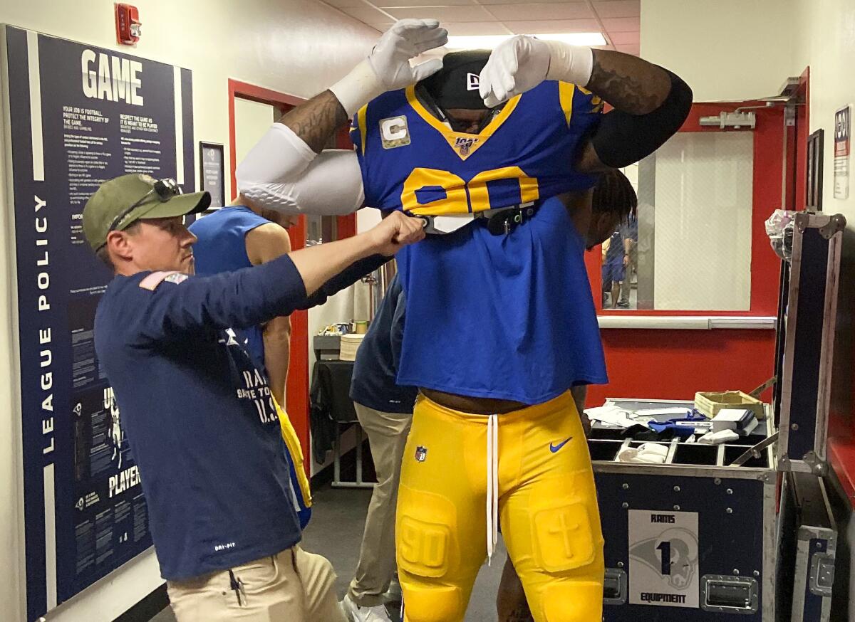 Assistant equipment manager Ben Bloomer helps Rams defensive tackle Michael Brockers pull on his pads before a Sunday night game against the Chicago Bears.