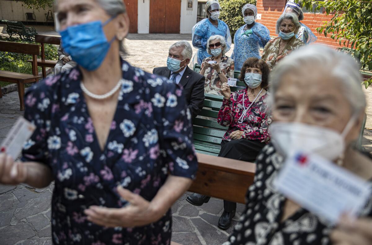 Reisents pose for a photo with their updated vaccination cards and Chilean Health Minister Enrique Paris after they were inoculated with their second dose of the Sinovac COVID-19 vaccine, on the patio of a home for the elderly in Santiago, Chile, Friday, March 5, 2021. No other country in Latin America has had anything near Chile's success in vaccinating its population. (AP Photo/Esteban Felix)