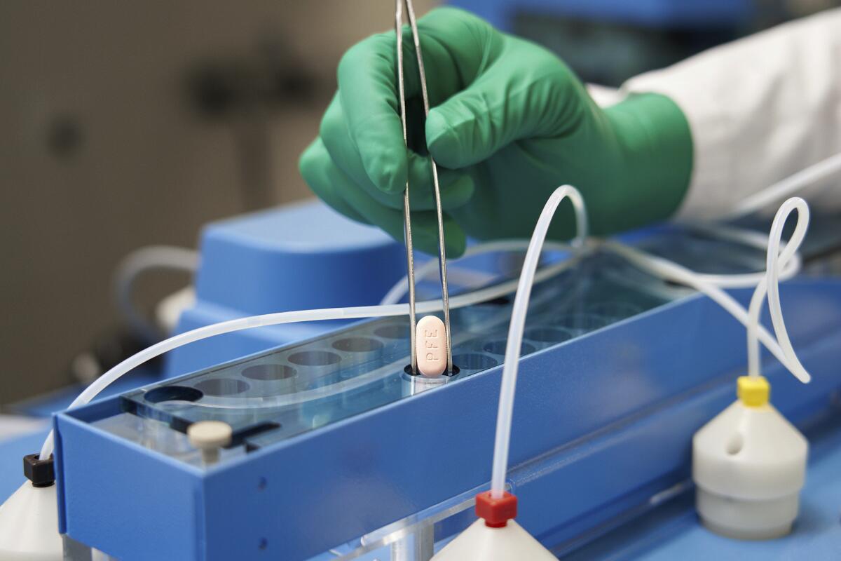 A gloved hand uses a pair of forceps to place pill into a tube 