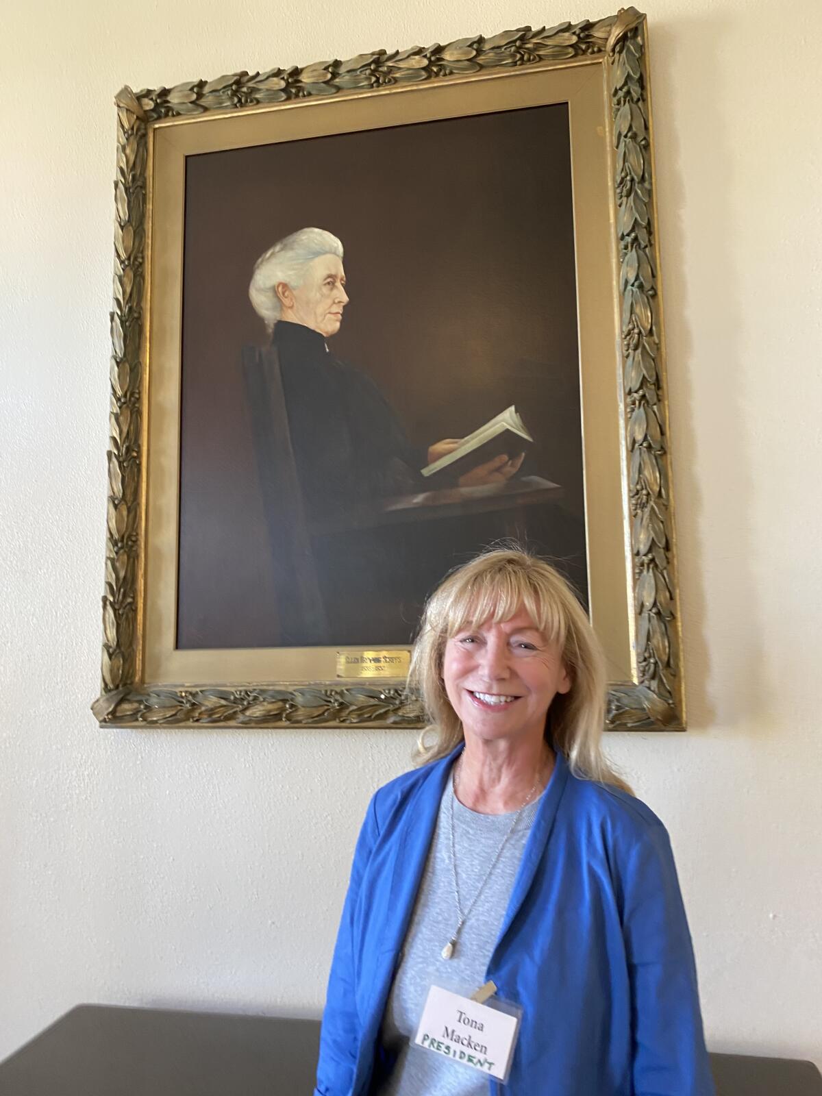 Tona Macken, president of the La Jolla Woman’s Club, poses beneath a painting of club founder, Ellen Browning Scripps, in its lobby.