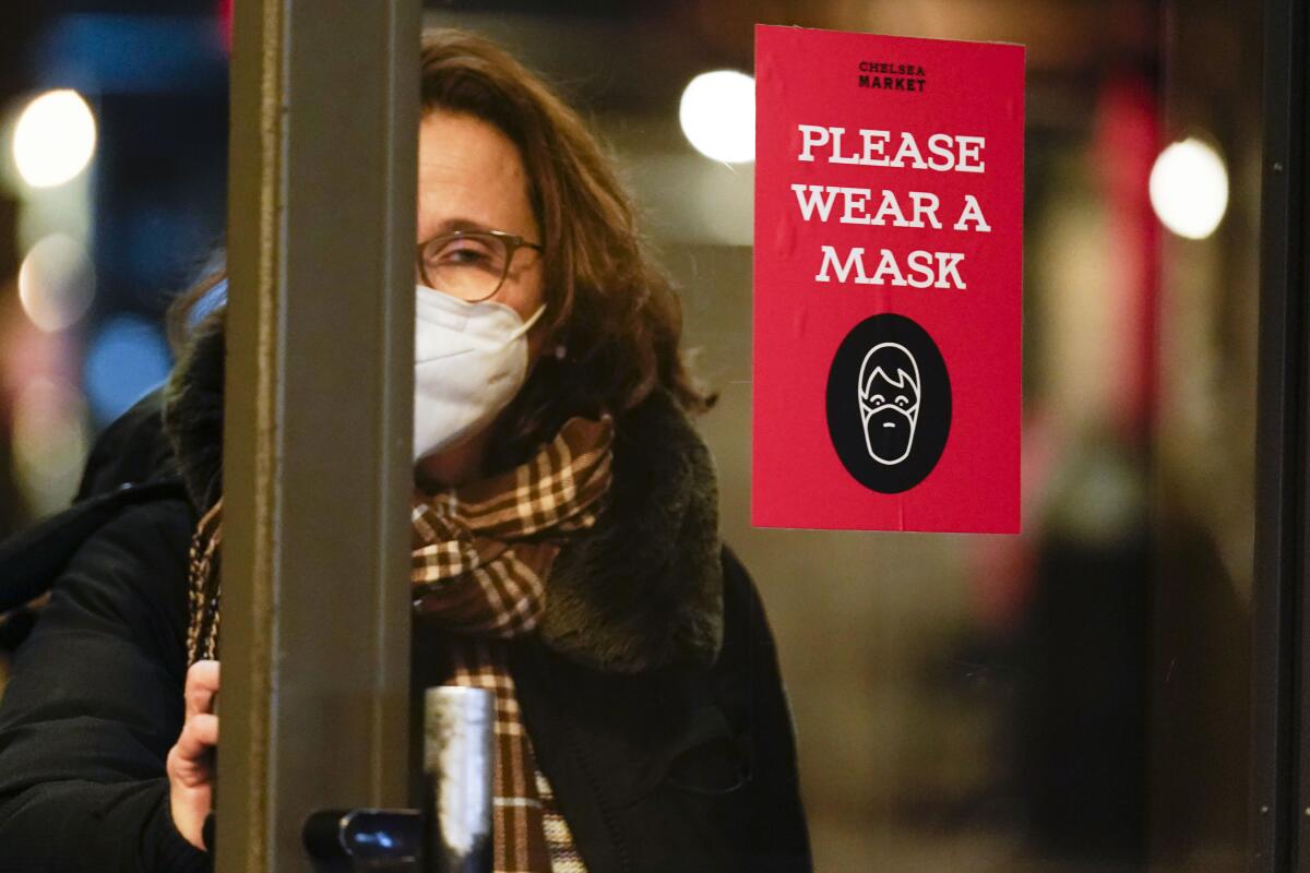 ARCHIVO - Una mujer pasa una puerta en la que se pide a los clientes que usen mascarilla, Nueva York,