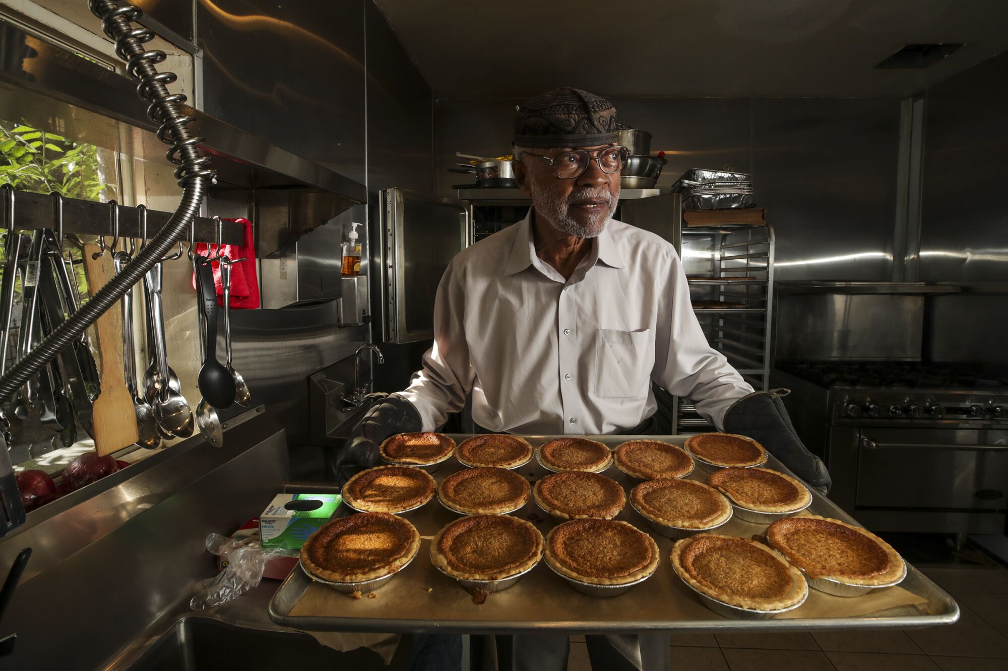 A man holds a tray of small pies in a kitchen  