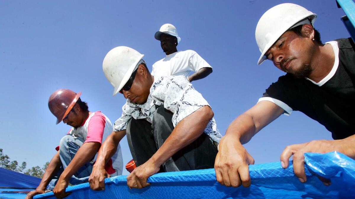 Immigrant workers install a plastic tarp as temporary protection for a home damaged by Hurricane Katrina in Gulfport, Miss. on Oct. 23, 2005.