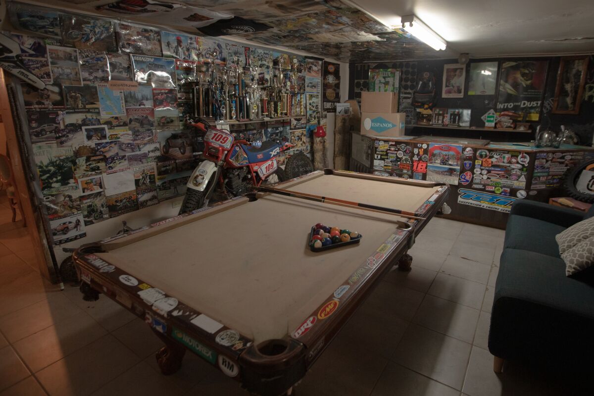 A room with a pool table in the center and a dirt bike against the wall, which is covered in photos and a shelf of trophies.