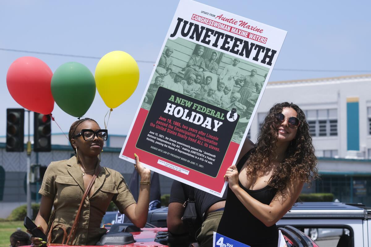 People hold up a sign about Juneteenth during a car parade.