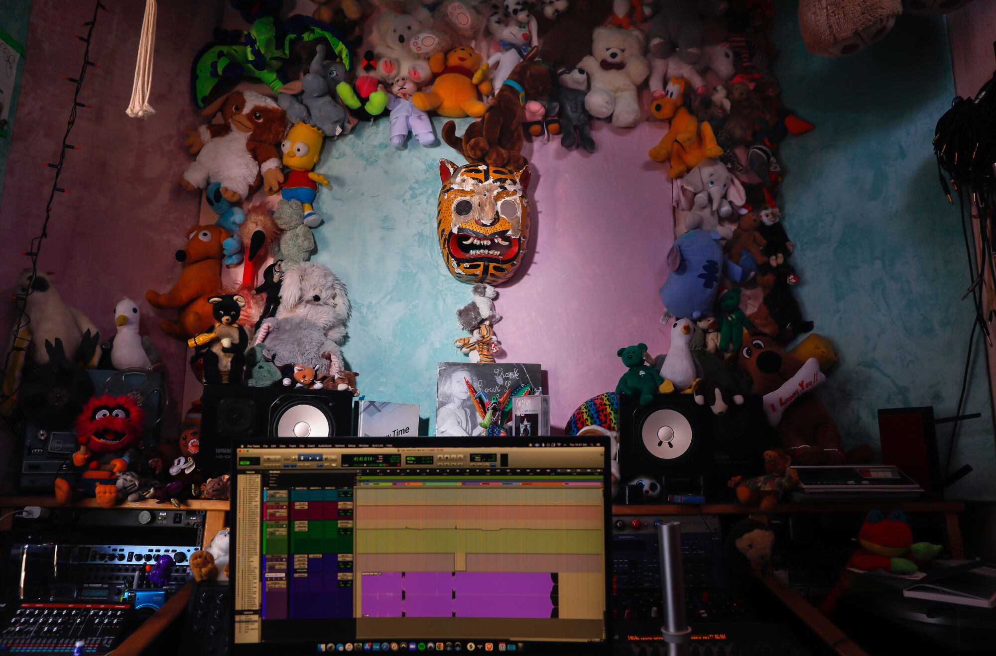 Stuffed animals hang against a pink and blue wall above a sound deck in a recording studio