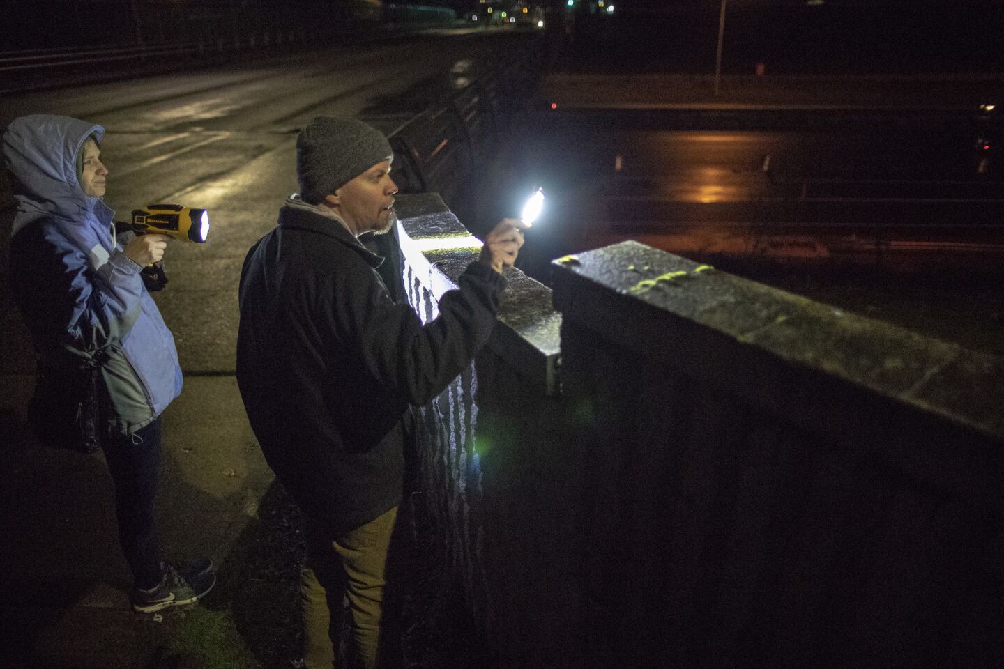 Members of the Montavilla Initiative citizens group Evelyn Macpherson, left, and Jeff Church shine flashlights toward a pair of tents pitched on an embankment alongside Interstate 205 while on patrol in their neighborhood in Portland, Ore.