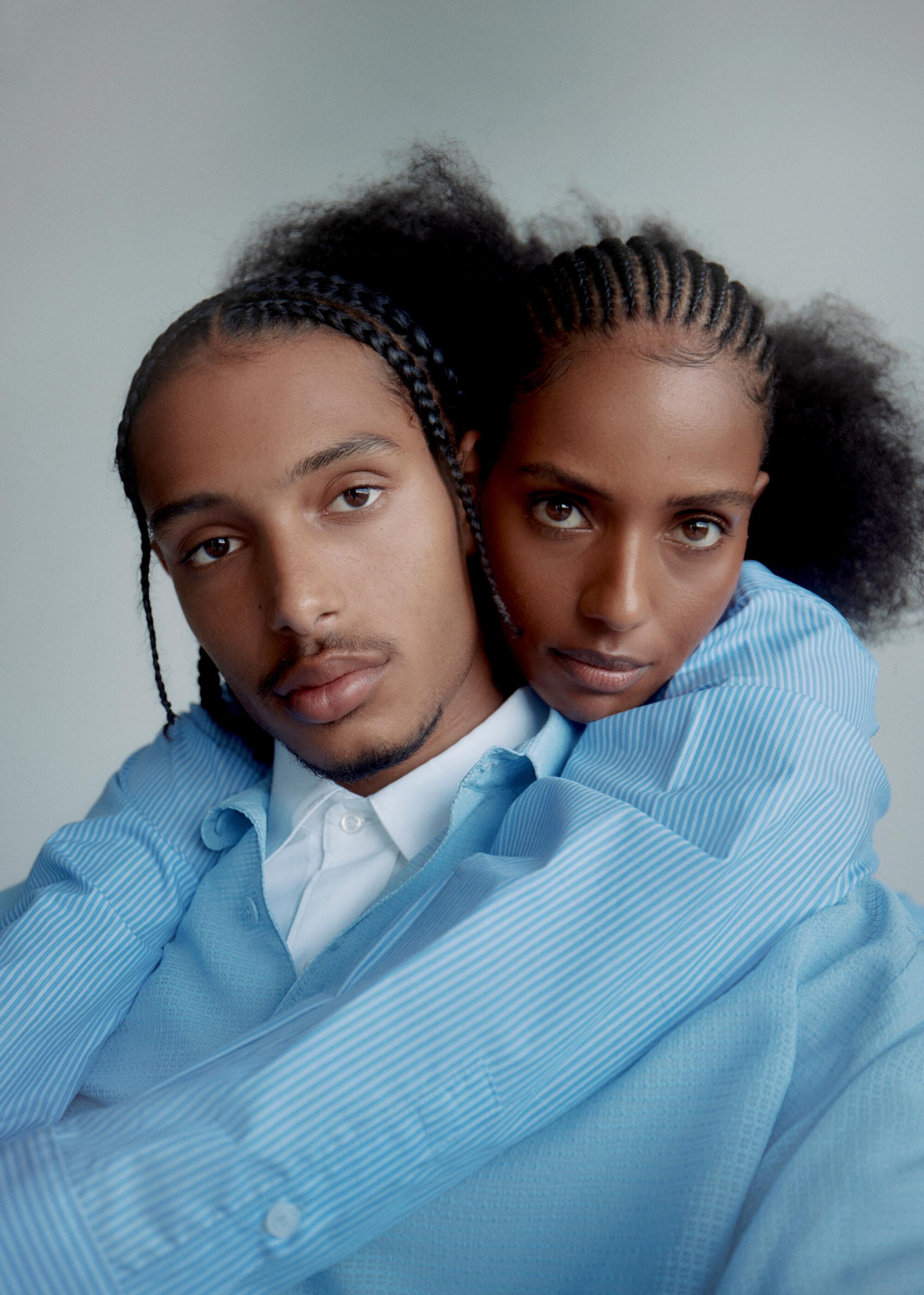 Two models wearing baby blue collared shirts embrace.