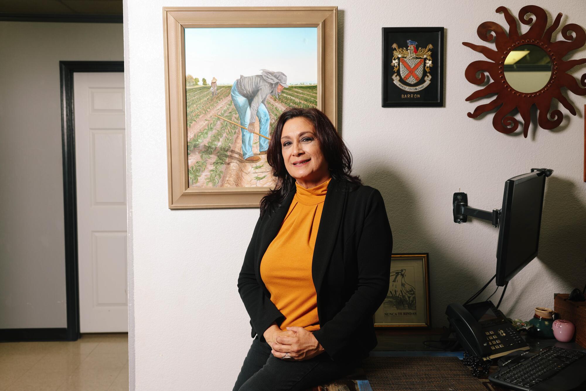 A woman in business attire poses in front of a farmworker painting. 