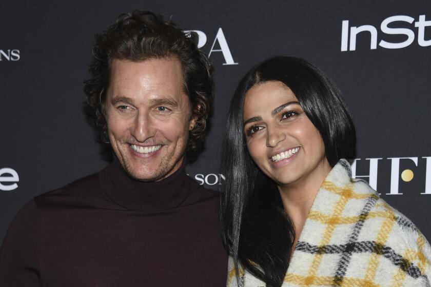 Matthew McConaughey smiling in a purple turtleneck next to Camila Alves in a plaid blanket