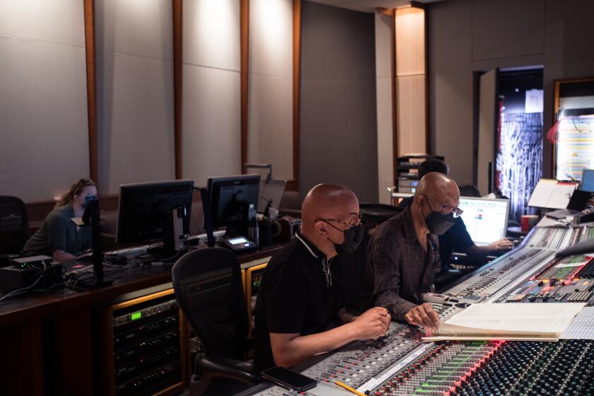 Rickey Minor and Booker White, both wearing face masks, supervise a sound board in a recording studio