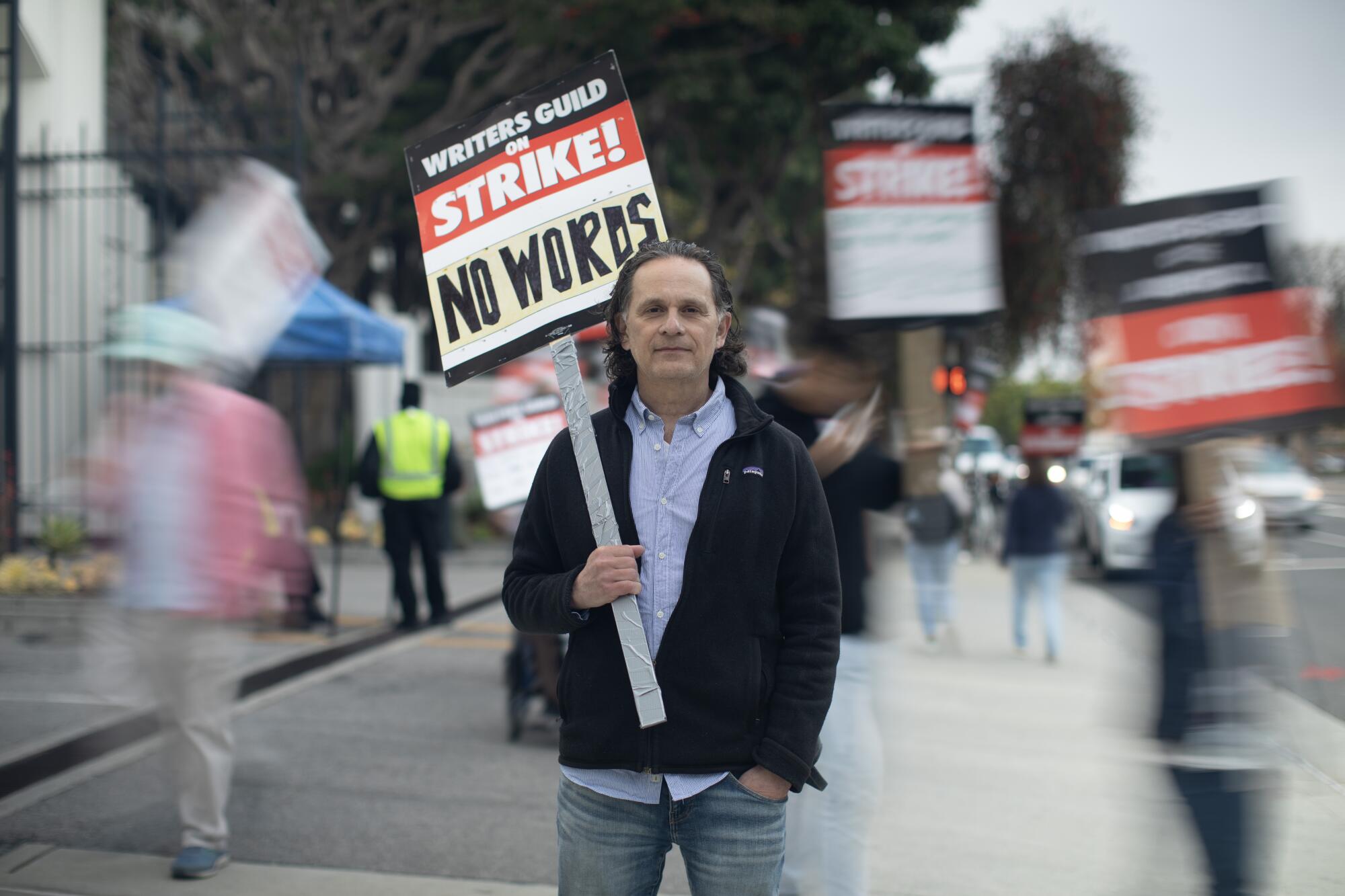 A man holds a Writers Guild strike sign reading "No Words."