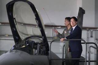 A man in uniform and another in suit and tie stand near the cockpit of a fighter jet with its canopy open