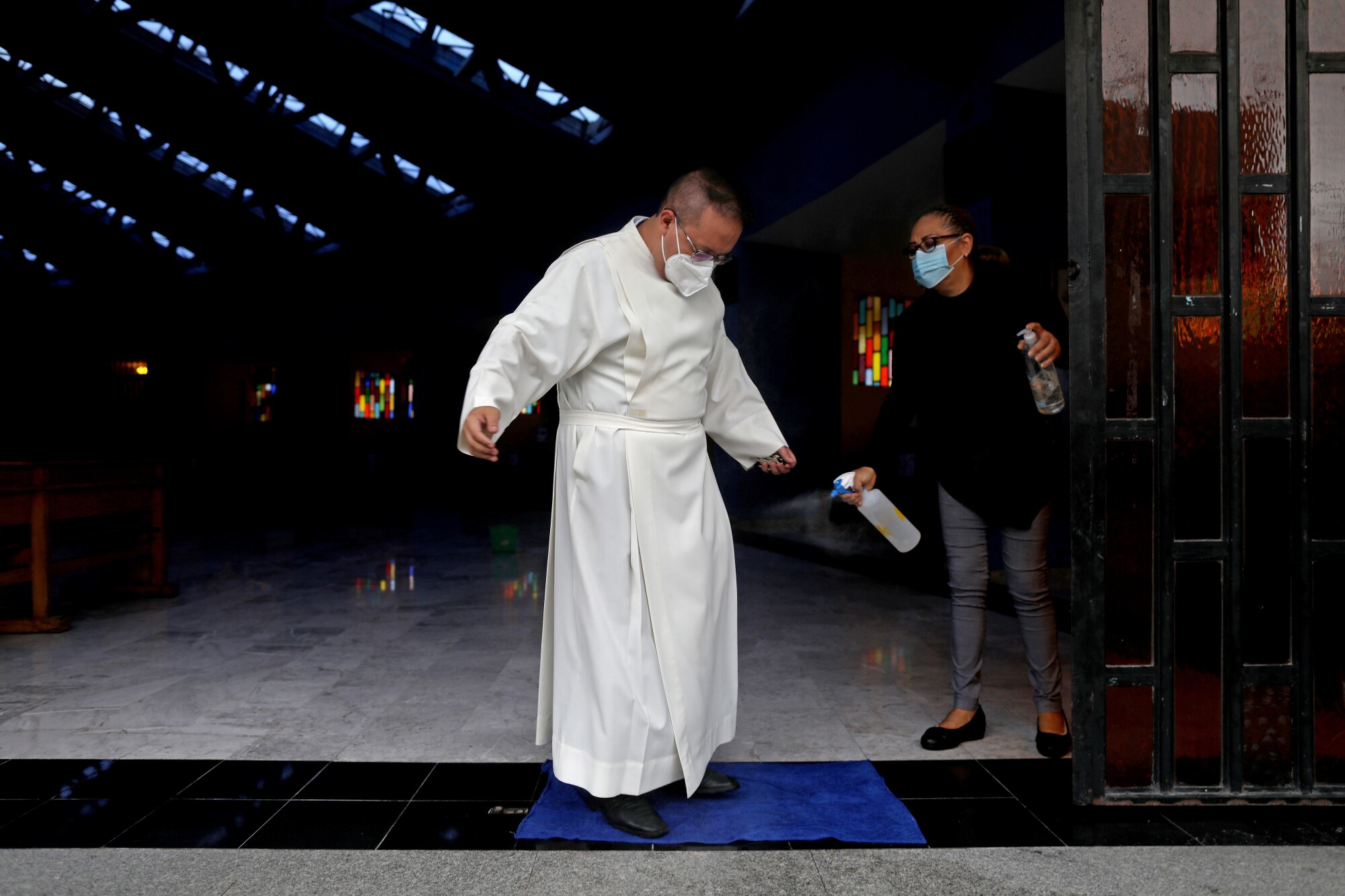 A woman sprays disinfectant on a priest in white robes