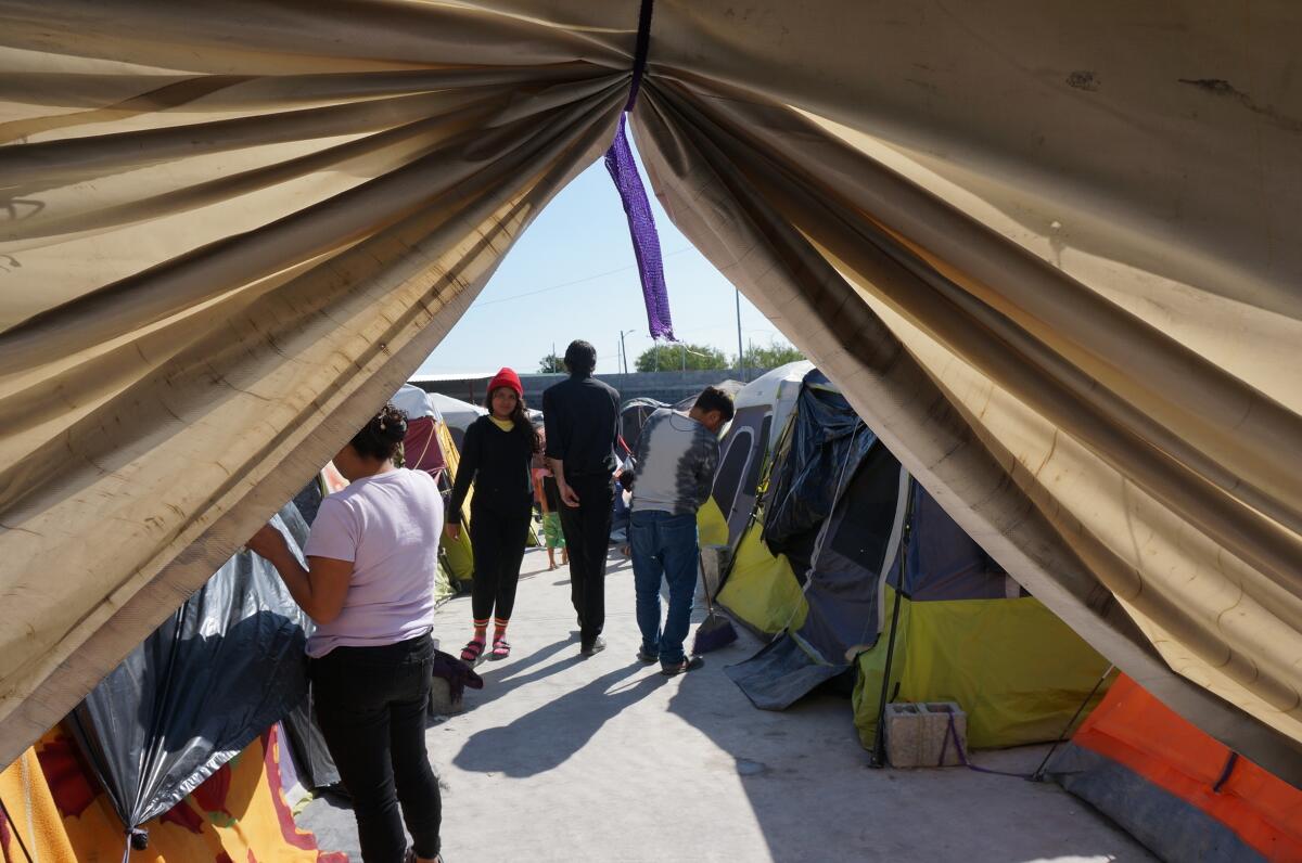 A view from inside a tent of people milling around several other tents in the sunshine.