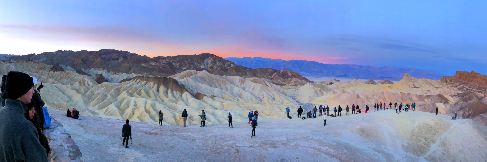Hikers watch sunrise over stark hills. Zabriskie Point, Death Valley National Park.