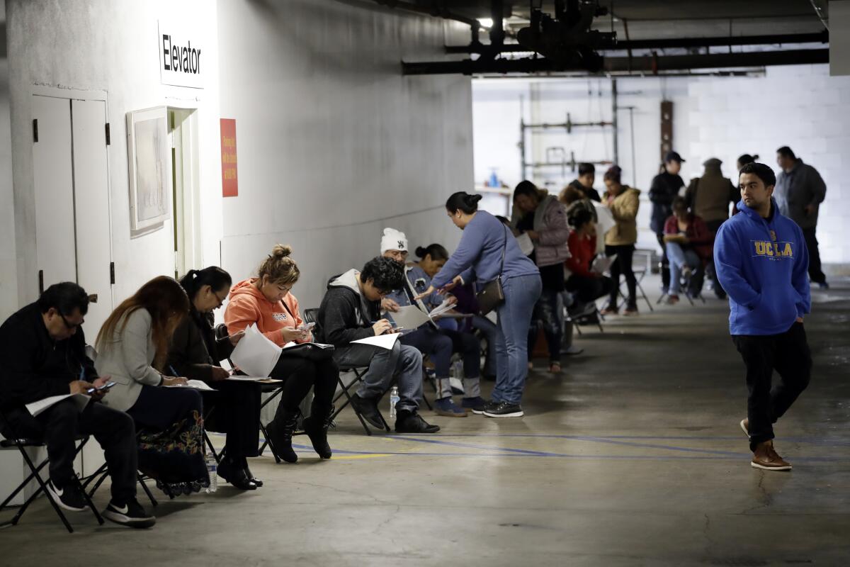 A line of people sitting in folding chairs while filling out forms in a parking garage