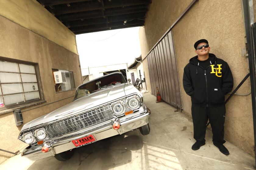 LONG BEACH, CA - AUGUST 10, 2021 - Jonathan Rodriguez, 20, stands next to his 1963 Impala SuperSport lowrider at Speedy's Metal Finishing in Long Beach on August 10, 2021. Rodriguez did most of the updates to his car at the place owned by his father, Luis "Speedy" Rodriguez. "During quarantine I would spend a lot of time doing upgrades to the car," said Jonathan. He added new batteries, added new coils, changed to one-way hydraulics and fixed the convertible top. Jonathan is a member of, "High Class Car Club," which was co-founded by his father. California's aftermarket industry, which is the largest in the nation flourished during the pandemic. It's made up of companies that help people modify their cars to help them go faster, run more efficiently, corner better, brake shorter and look better. These companies did record business in 2020 keeping up with owners like Rodriguez. (Genaro Molina / Los Angeles Times)