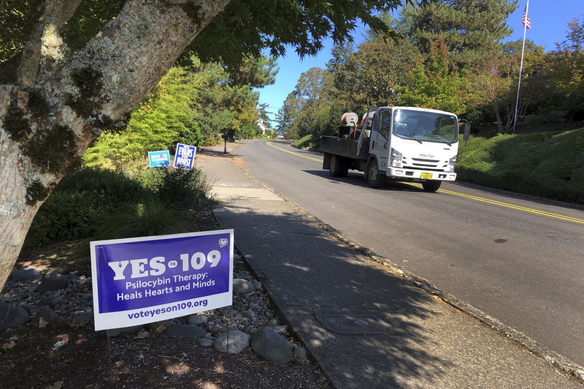 A truck drives past a sign supporting a ballot measure that would legalize controlled, therapeutic use of psilocybin mushrooms, Friday, Oct. 9, 2020 in Salem, Ore. War veterans with PTSD, terminally ill patients and others suffering from anxiety are backing the ballot measure. (AP Photo/Andrew Selsky)