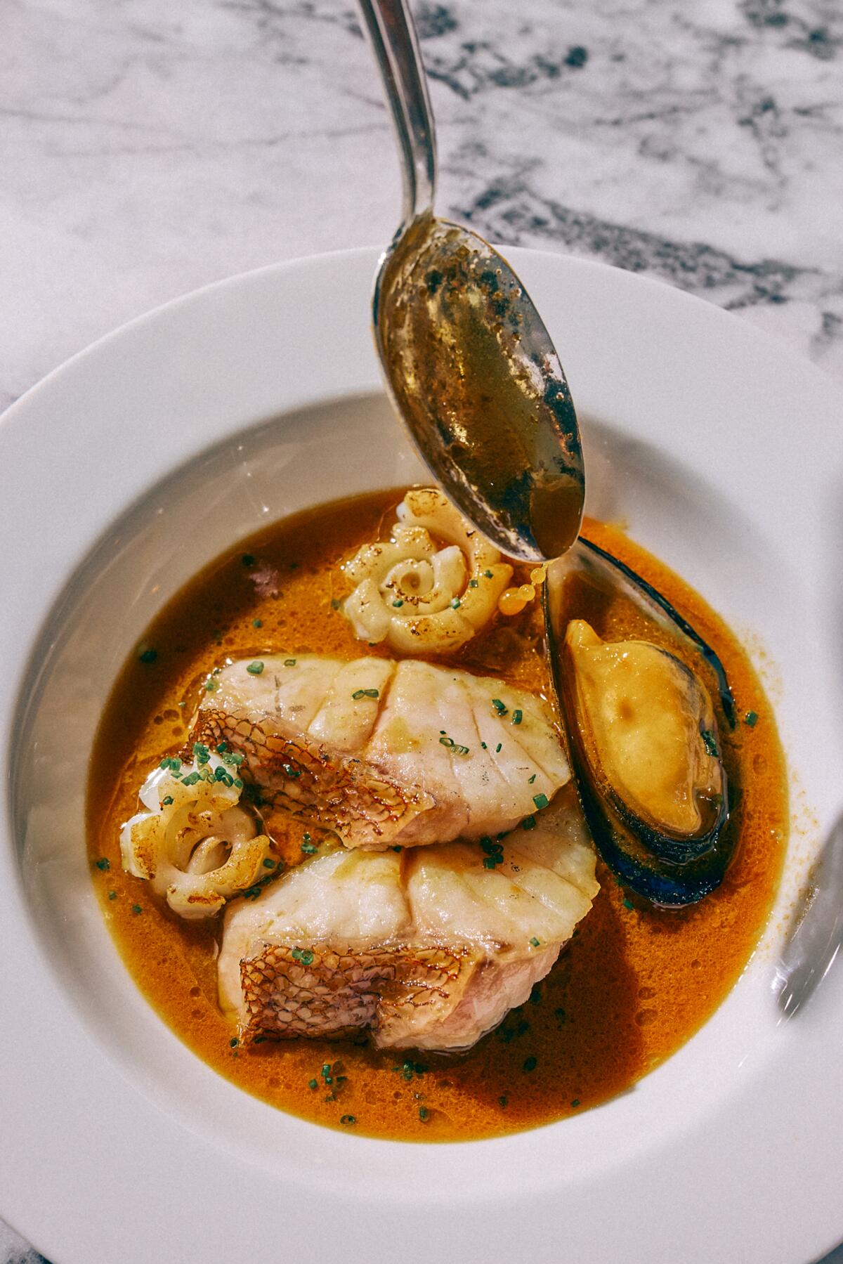 A photo of a spoon ladling sauce atop rockfish in a white bowl