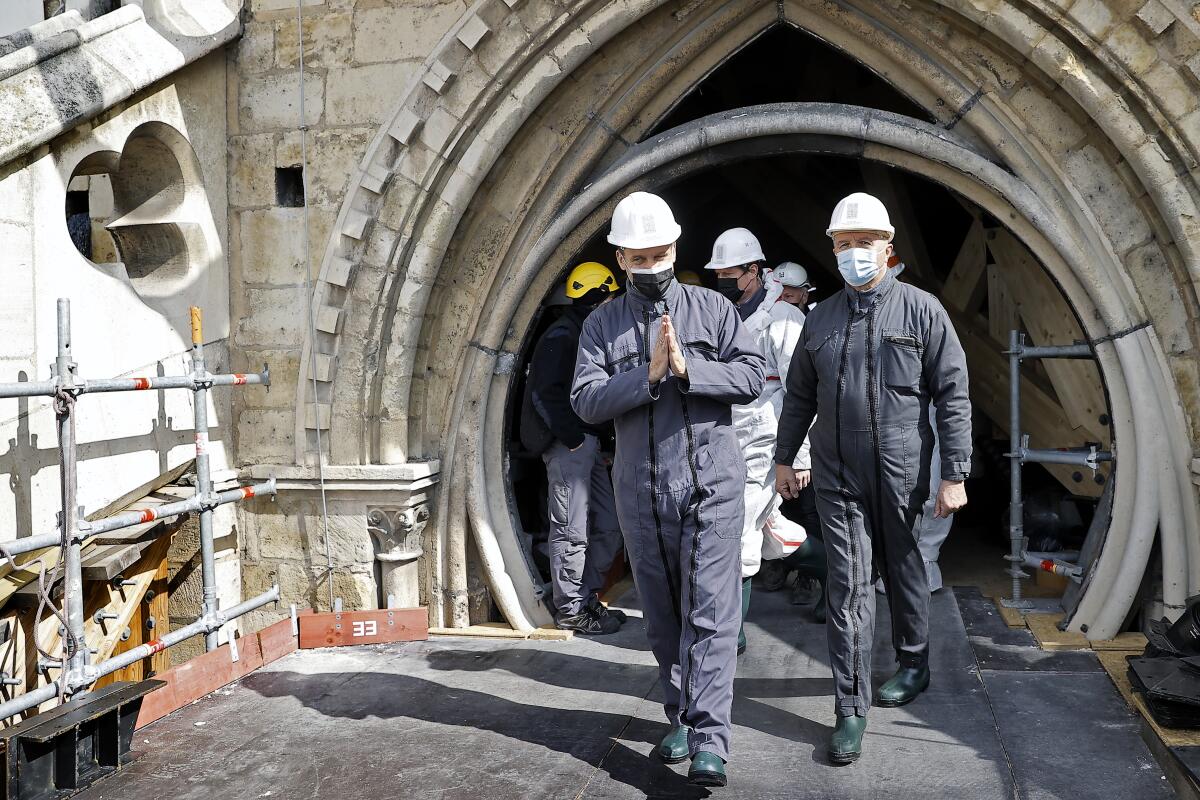 Two men in overalls walk on a construction scaffolding before a Gothic arch