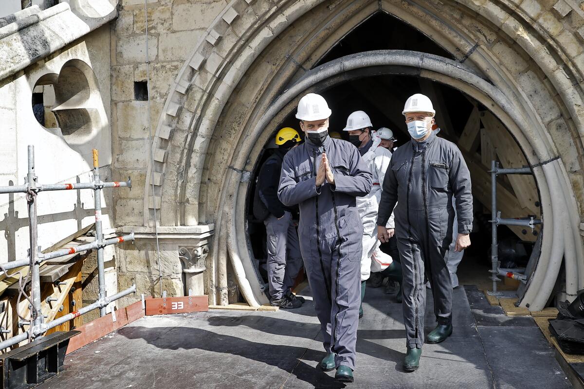 Two men in overalls walk on a construction scaffolding before a Gothic arch 