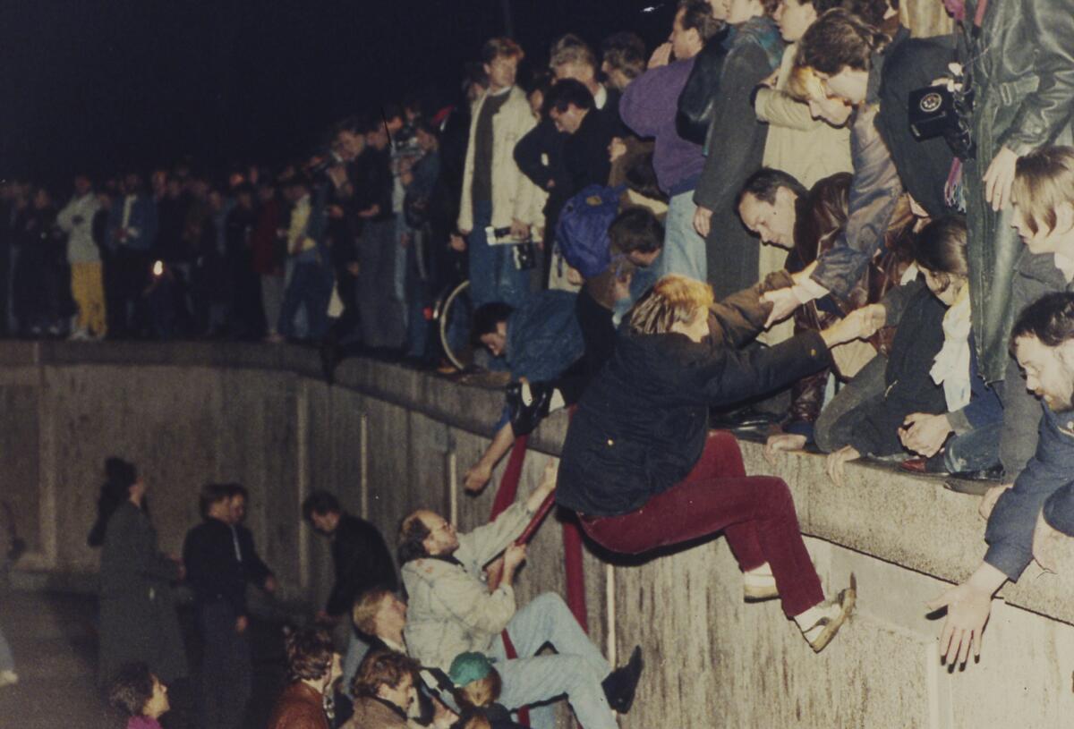 East Berliners get helping hands from West Berliners as they climb the Berlin Wall.
