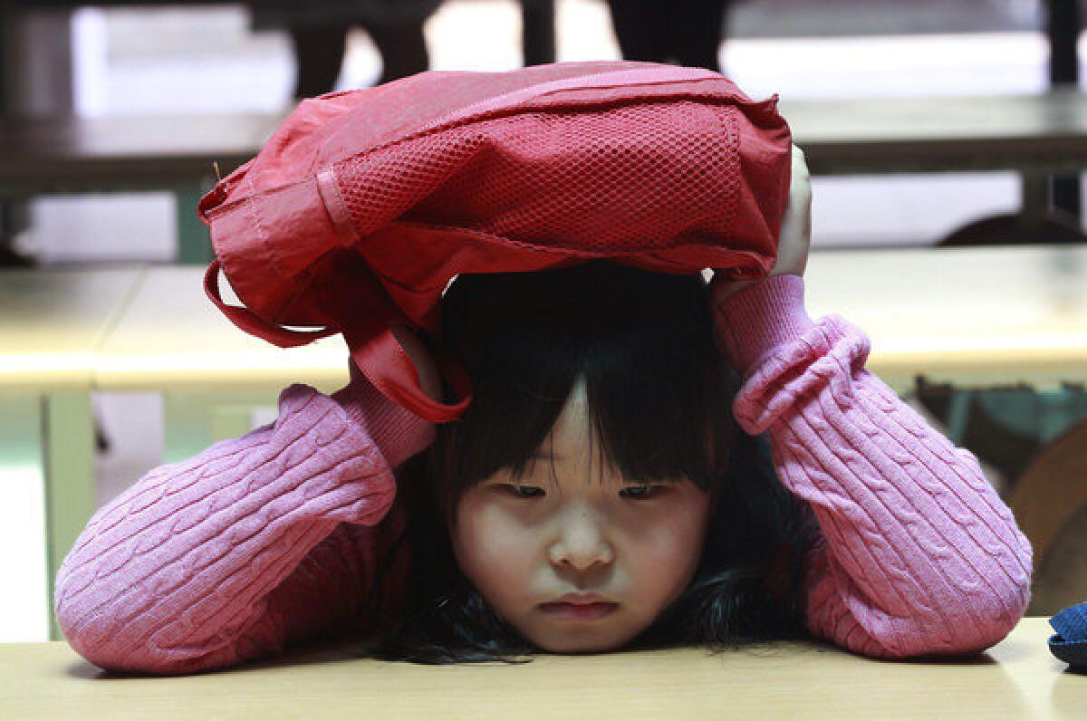 A South Korean elementary school student covers her head with a school bag at an underground shelter Tuesday during a drill for a possible airstrike at Sohwa elementary school in Paju near the border with North Korea.