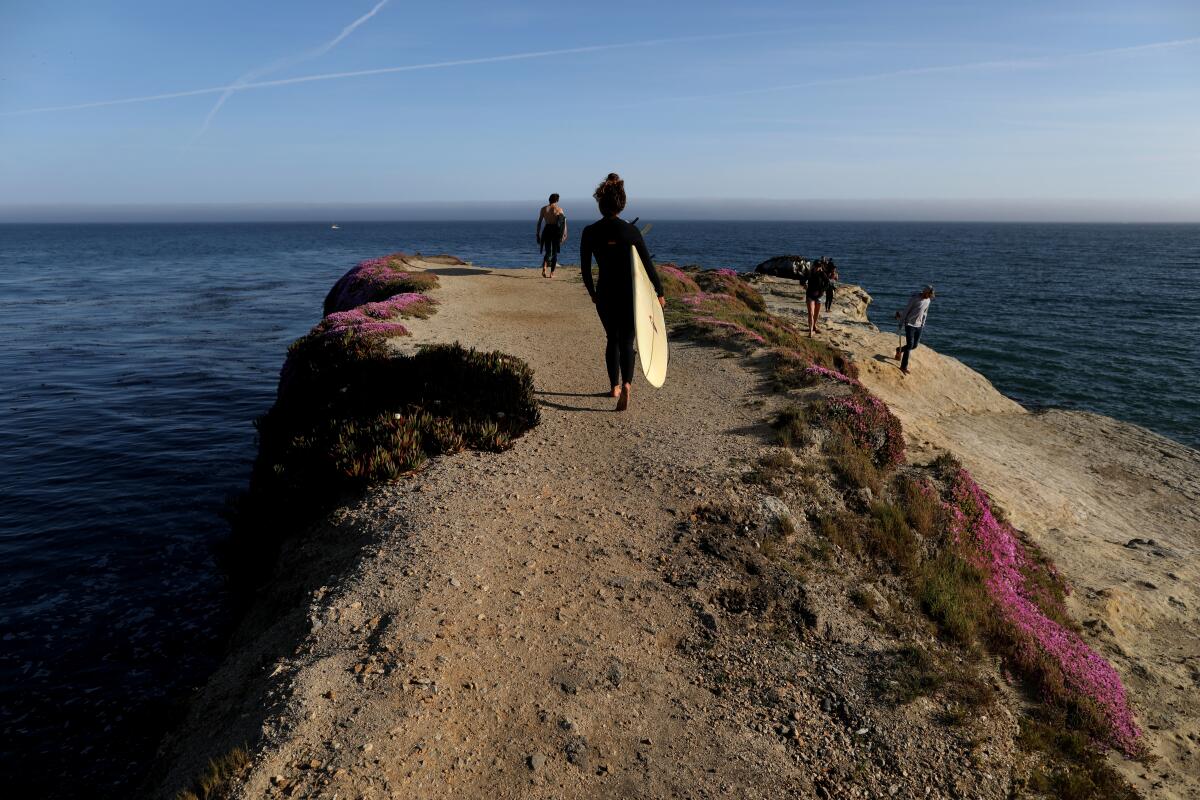 Quinn Comer and Alyssa Anzalone walk to the end of Lighthouse Point in Santa Cruz to jump into the surf on Friday, May 8. Times photographer Gary Coronado went to the idyllic seaside town to give us this visual report on one of the state’s beautiful areas in the time of the coronavirus.