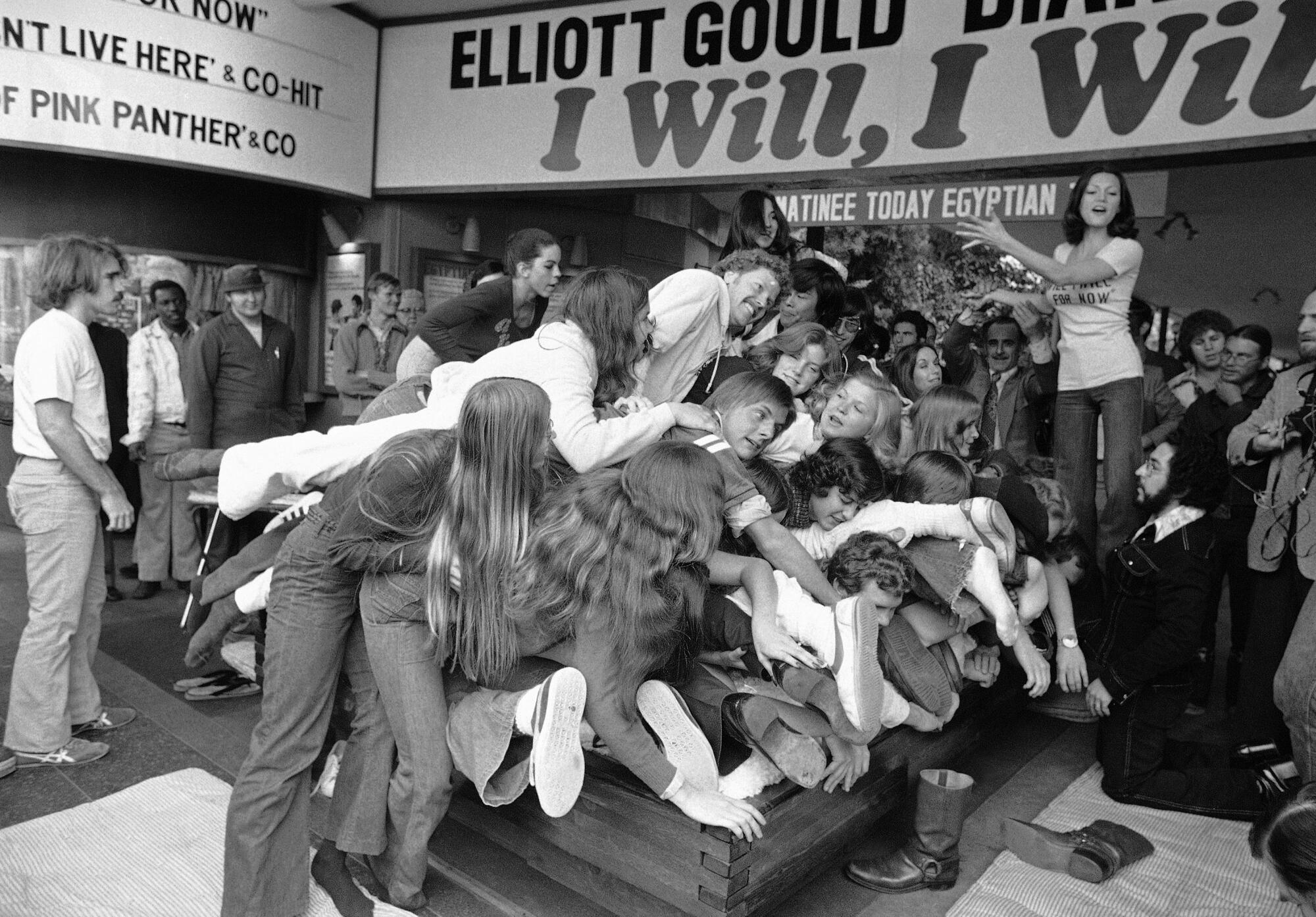 A black-and-white photo of several college-age people lying in a pile on a waterbed.