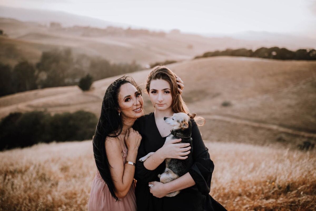 Two people pose in a field. One holding a dog