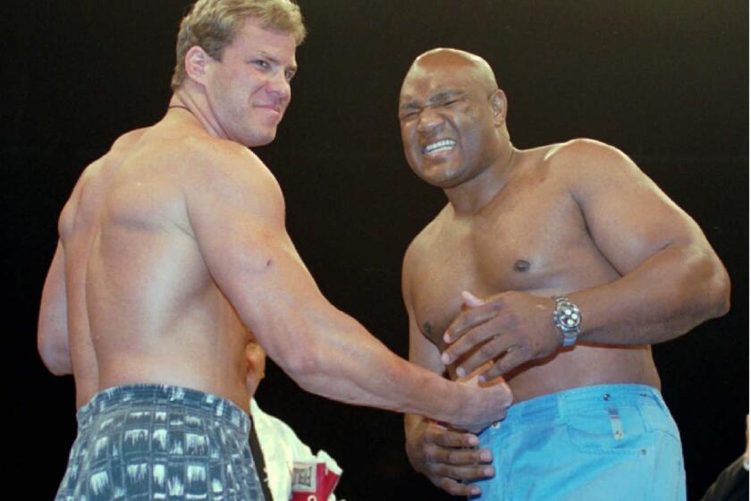 George Foreman, right, grimaces as Tommy Morrison delivers a fake punch as the two boxers joke around while promoting their 1993 bout.
