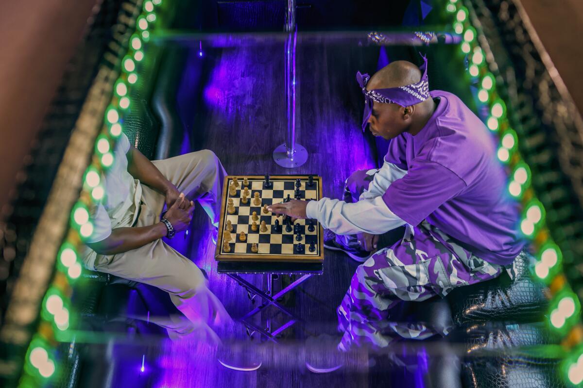 A man wearing a purple shirt and purple bandana on his head plays chess under purple and green lights