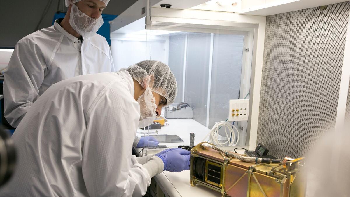Austin Kruggel, left, and Vidur Kaushish, employees of Tyvak Nano-Satellite Systems, Inc., place a CubeSat, or nano-satellite, into a dispenser on July 26.