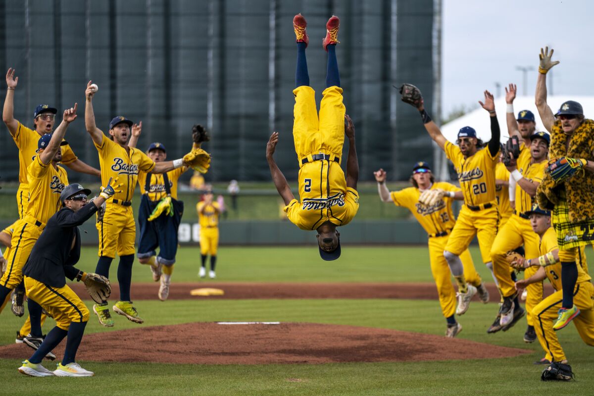 Malachi Mitchell wears a yellow uniform and flips in the air above the pitcher's mound as his teammates cheer.