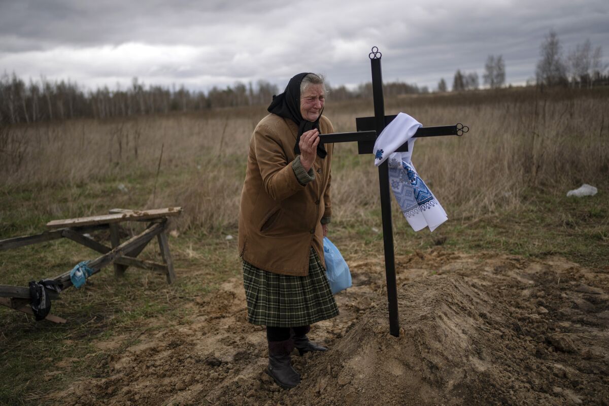 Nadiya Trubchaninova, 70, cries while holding the cross of her son Vadym, 48, who was killed by Russian soldiers last March 30 in Bucha, during his funeral in the cemetery of Mykulychi, on the outskirts of Kyiv, Ukraine, Saturday, April 16, 2022. After nine days since the discovery of Vadym's corpse, finally Nadiya could have a proper funeral for him. This is not where Nadiya Trubchaninova thought she would find herself at 70 years of age, hitchhiking daily from her village to the shattered town of Bucha trying to bring her son's body home for burial. (AP Photo/Rodrigo Abd)