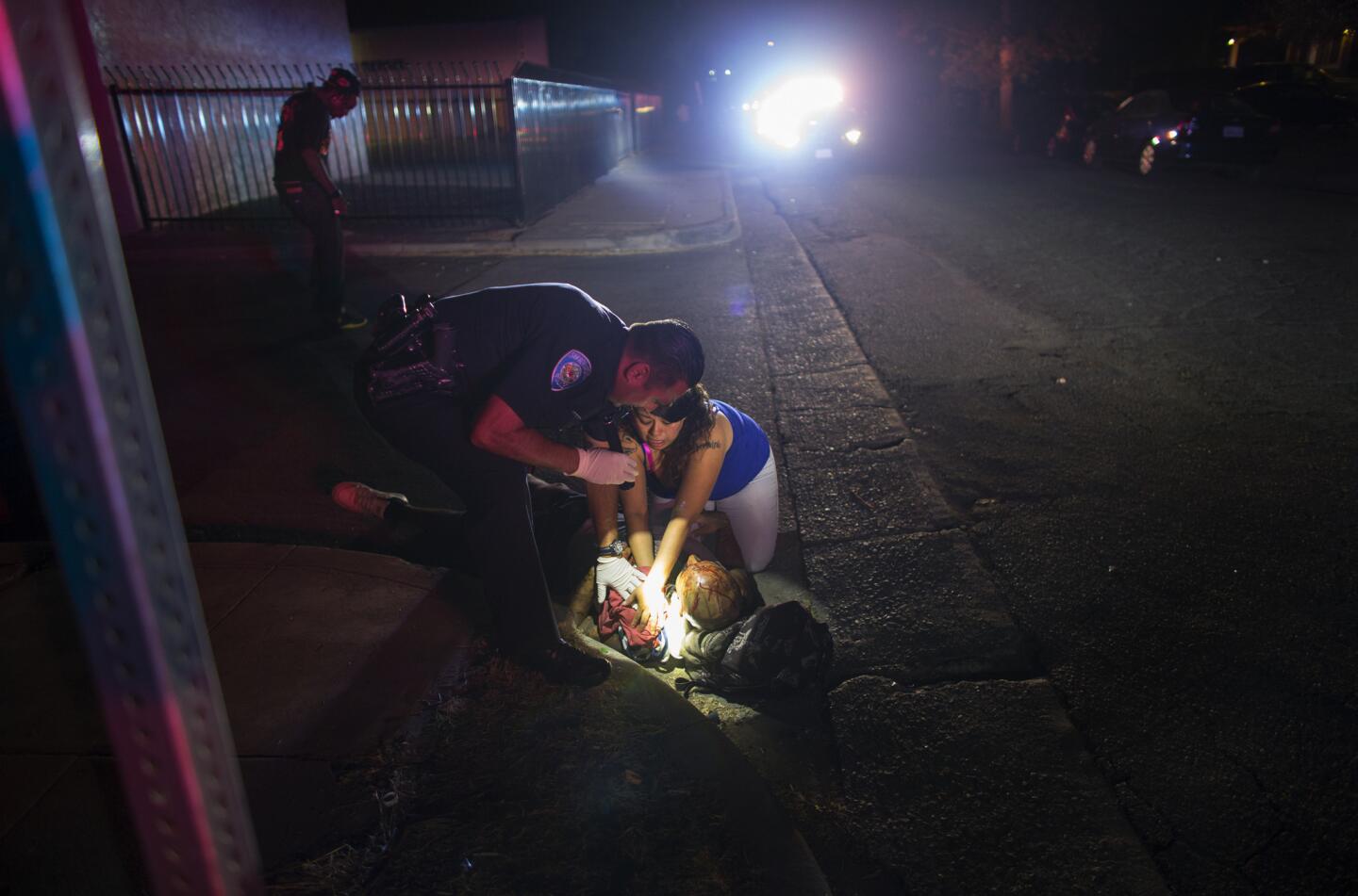 A San Bernardino police officer assists as a resident tries to stop the bleeding of a male gunshot victim found lying next to the curb after being shot with a shotgun at the intersection of 11th Street and Acacia Avenue on July 29, 2016. There have been 150 shootings and 47 homicides so far this year in the city. This victim survived, but declined to identify who shot him.