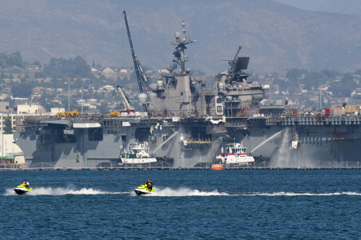 Boats spray water onto a Navy warship as people ride personal watercraft in the foreground