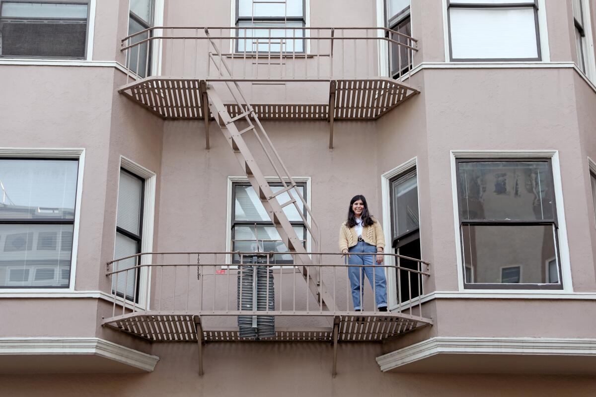 A woman stands on a balcony of an apartment building. 