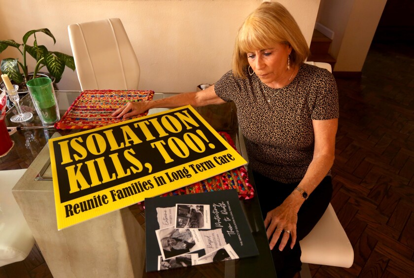 Karen Klink sits next to a sign ("Isolation Kills, Too!") she used in protest when it was hard to visit her mother. 