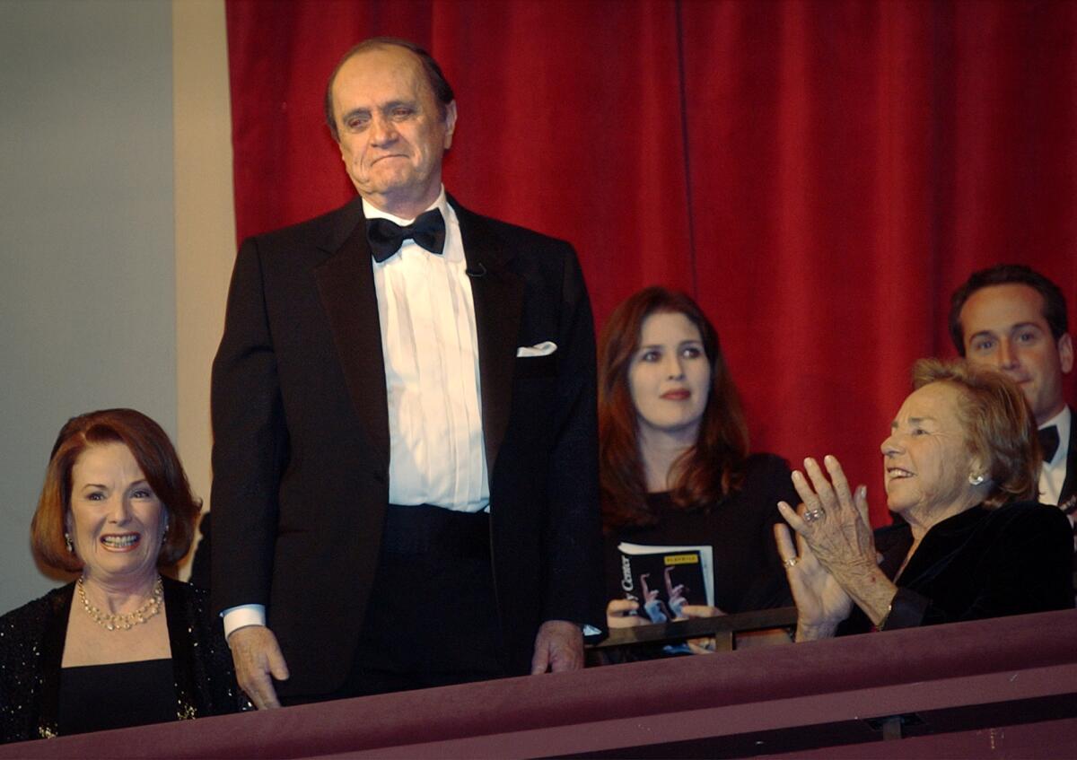 Bob Newhart standing in a tuxedo on a theater balcony with other guests who are sitting