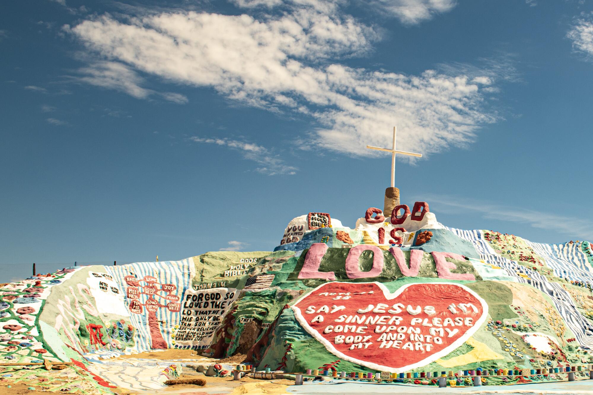 A small, colorful hill adorned with religious phrases and a crucifix affixed to its peak.