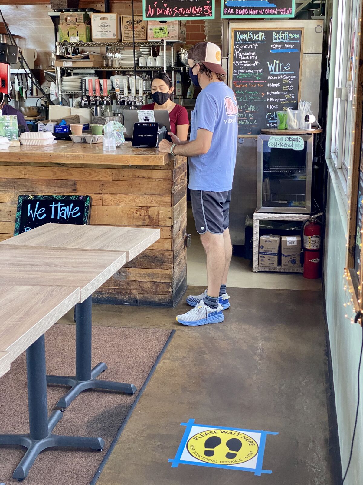 A masked employee serves a customer at La Jolla's Trilogy Sanctuary vegan cafe in May 2020.