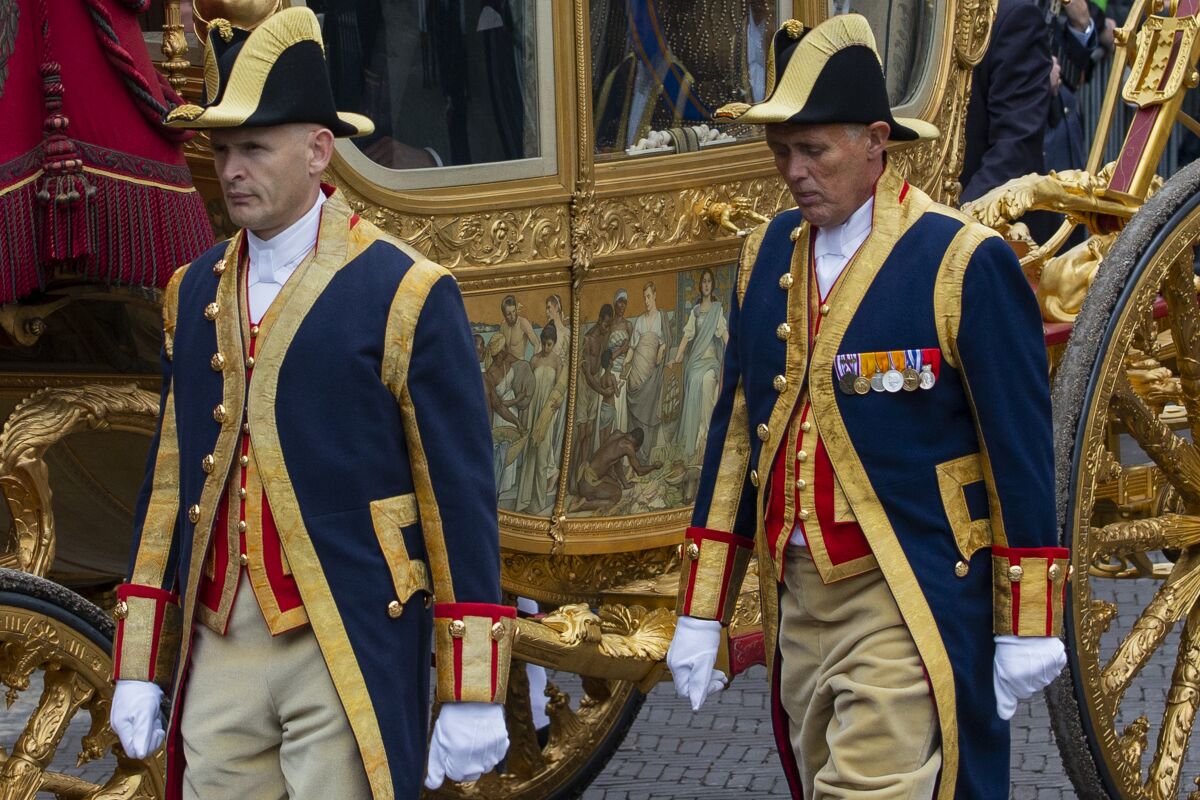 FILE- Footmen walk alongside the Golden Carriage as Netherlands' King Willem-Alexander and Queen Maxima arrive at Noordeinde Palace, after the King officially opened the new parliamentary year in The Hague, Netherlands, Tuesday Sept. 17, 2013. The Dutch king ruled out Thursday, Jan. 13, 2022, using in the near future the royal family's Golden Carriage, one side of which is decorated with a painting, center, that has drawn fire from critics who say it glorifies the Netherlands' colonial past, including its role in the global slave trade. (AP Photo/Peter Dejong, File)