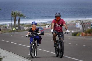 Wearing cloth face coverings and gloves, Neal Tricarico and son Anthony ride along Coast Highway in Encinitas on April 5, 2020. The CDC recommends wearing cloth face coverings while out in public. All beaches in San Diego County have been closed due to COVID-19.